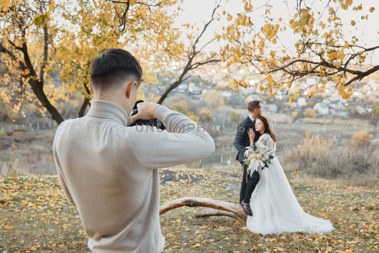 Professional wedding photographer taking pictures of the bride and groom in nature in autumn