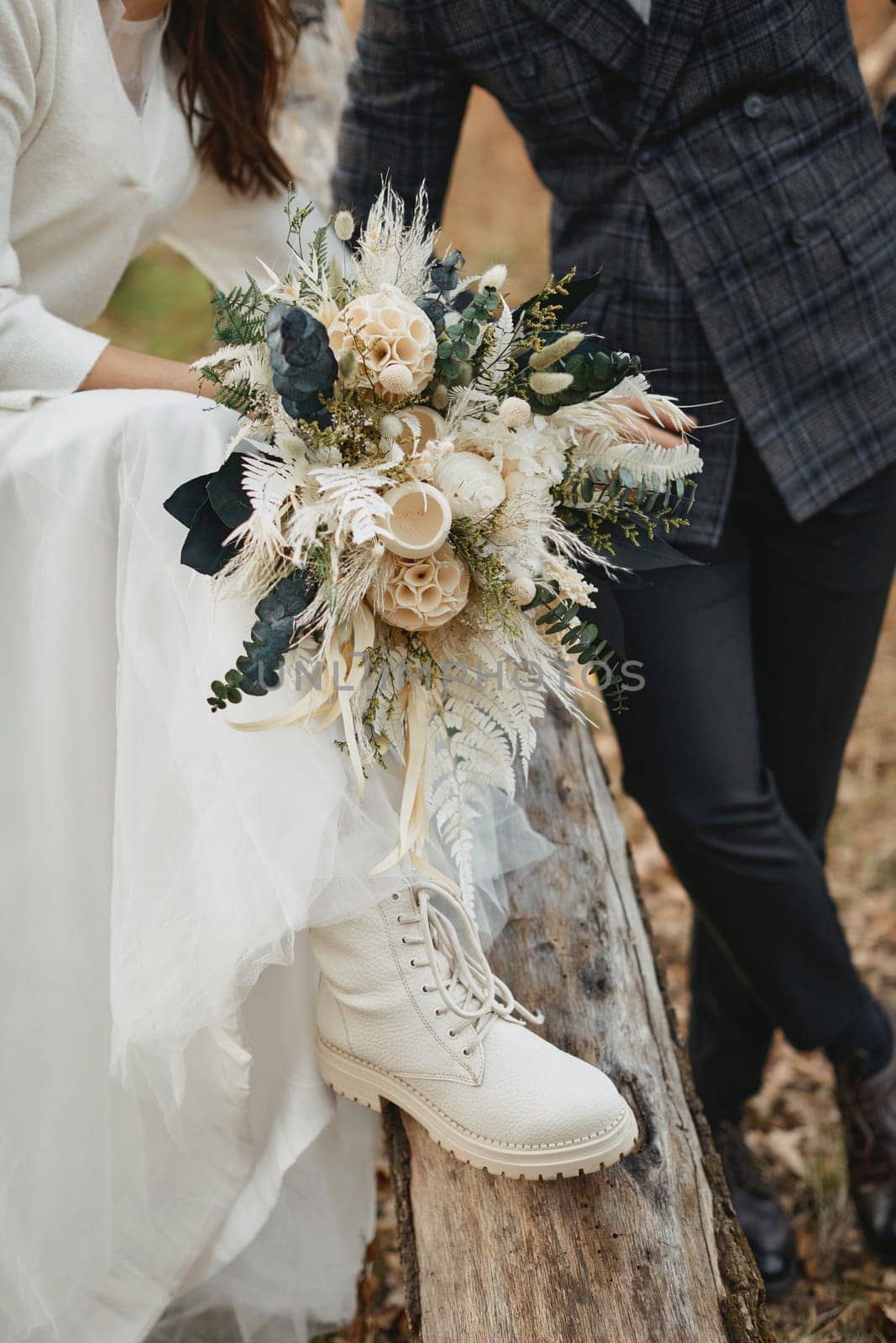 groom and bride wearing white boots holding beautiful autumn bouquet.