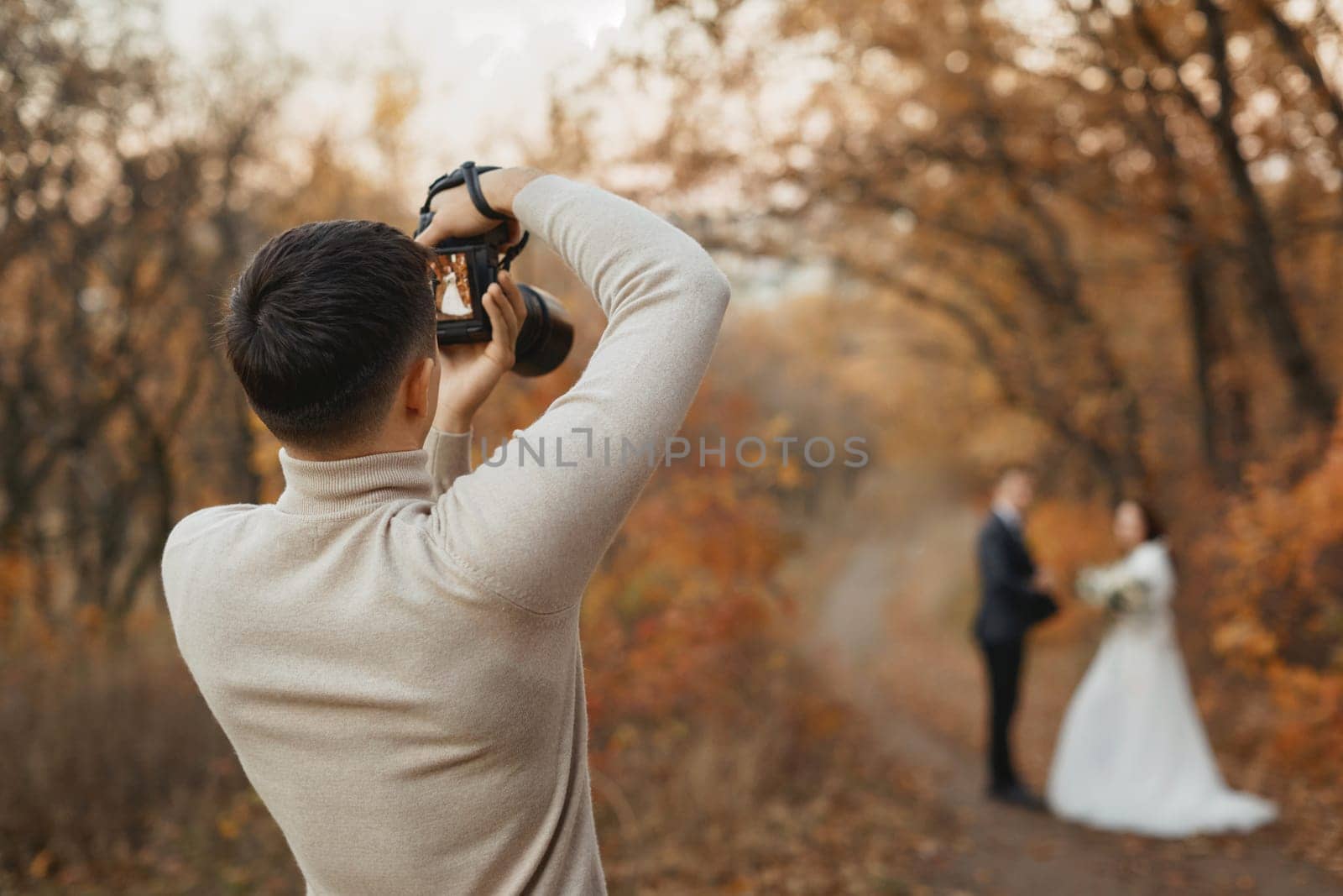 Professional wedding photographer taking pictures of the bride and groom in nature in autumn