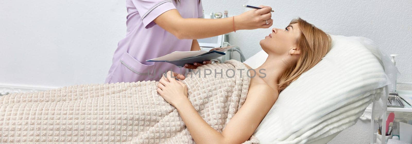 cosmetologist marking skin of caucasian woman with white pencil. facial marking for aesthetic procedure.