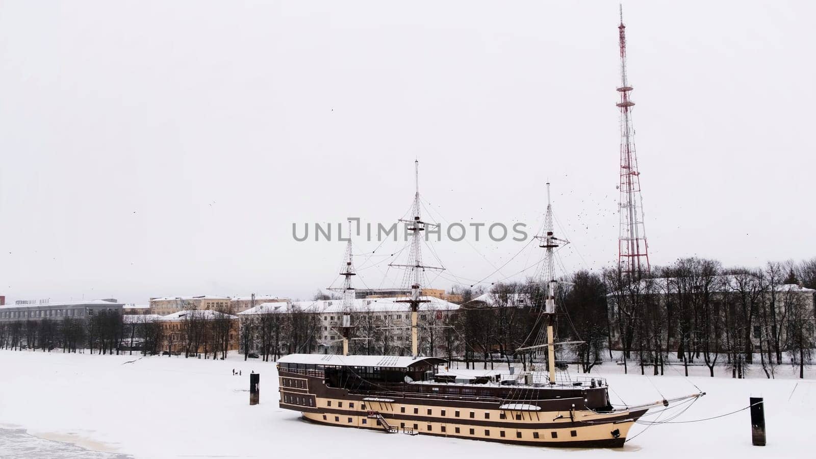 Floating restaurant Frigate Flagship on the Volkhov river on a winter day, Velikiy Novgorod. Concept. Beautiful retro stylized ship on a snow and ice covered river on cloudy sky background