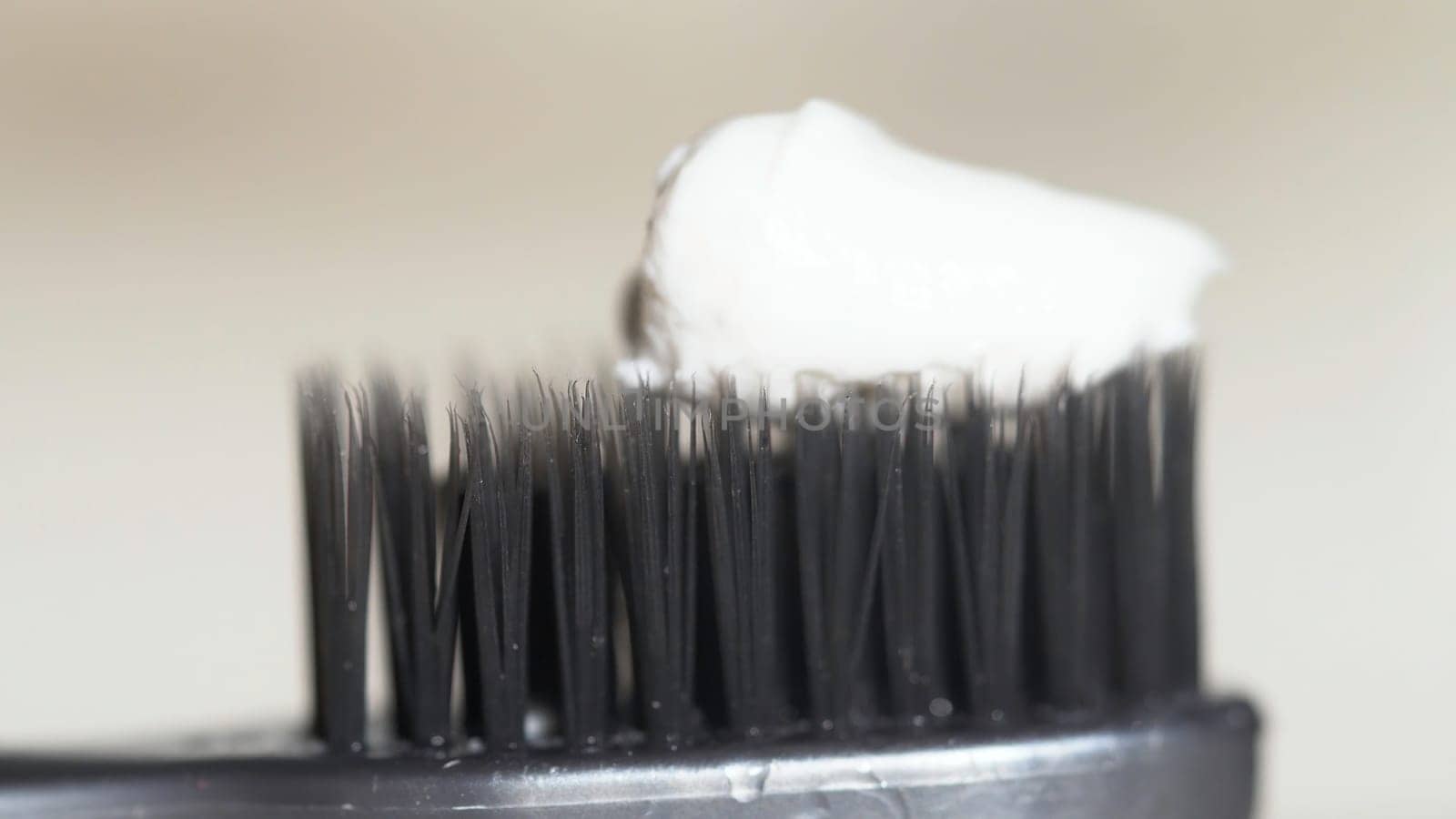 Extreme close up for a black toothbrush with white toothpaste being squeezed on it on beige background. The black bristles of the toothbrush with white toothpaste, dental care concept.