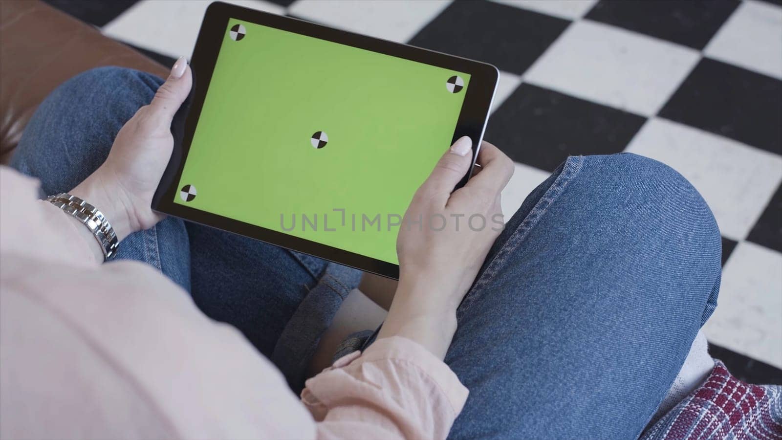 Young woman using black tablet device with green screen. Stock footage. Woman holding tablet, zooming pages while sitting on the couch in the living room. Chroma key. by Mediawhalestock