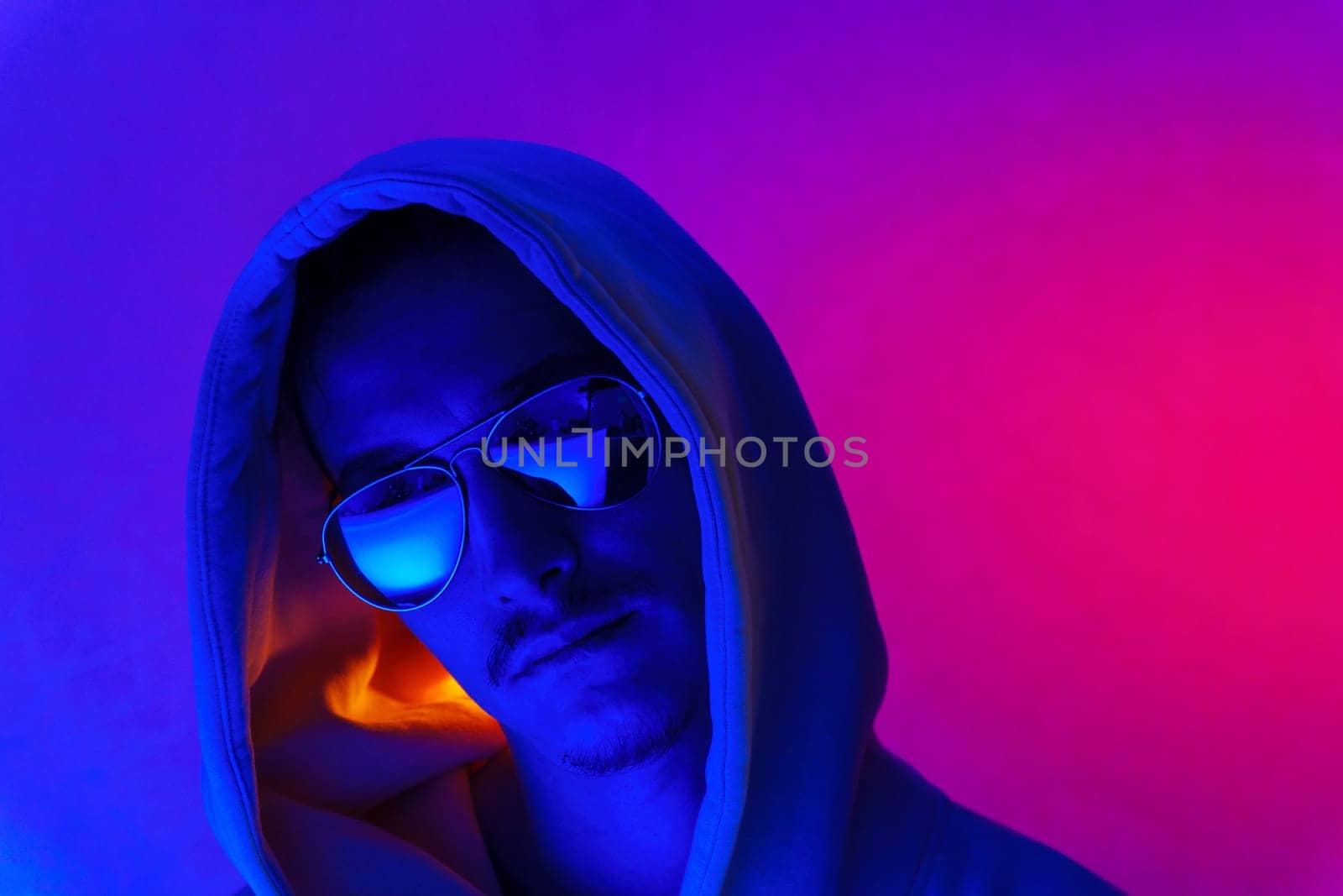 Portrait of a millennial man in neon light. Hipster in a hoodie. Selective focus