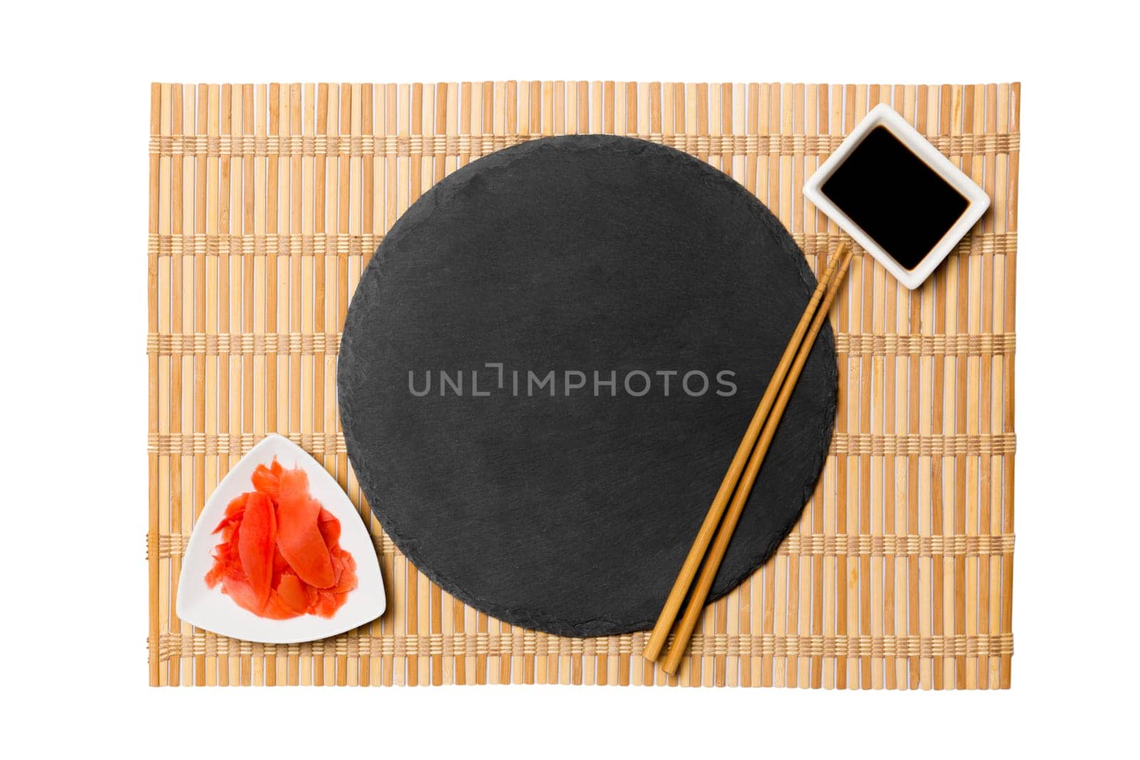 Emptyround black slate plate with chopsticks for sushi and soy sauce, ginger on yellow bamboo mat background. Top view with copy space for you design by Snegok1967