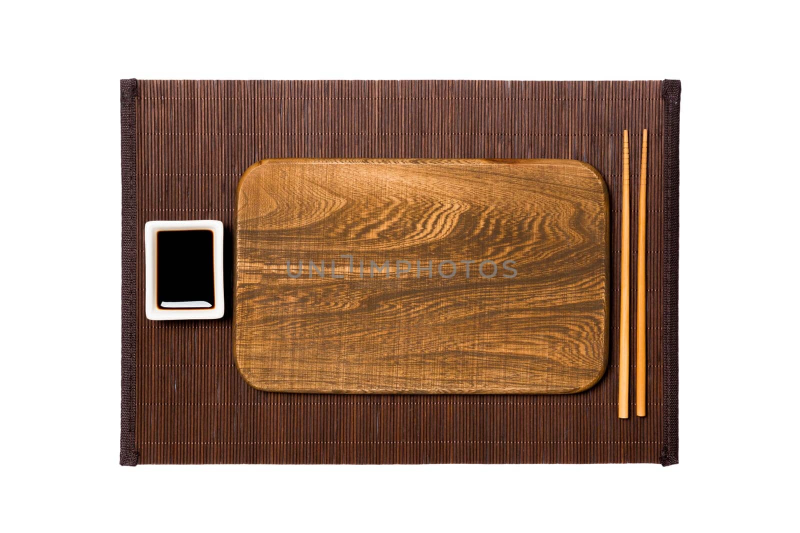 Empty rectangular brown wooden plate with chopsticks for sushi and soy sauce on dark bamboo mat background. Top view with copy space for you design.