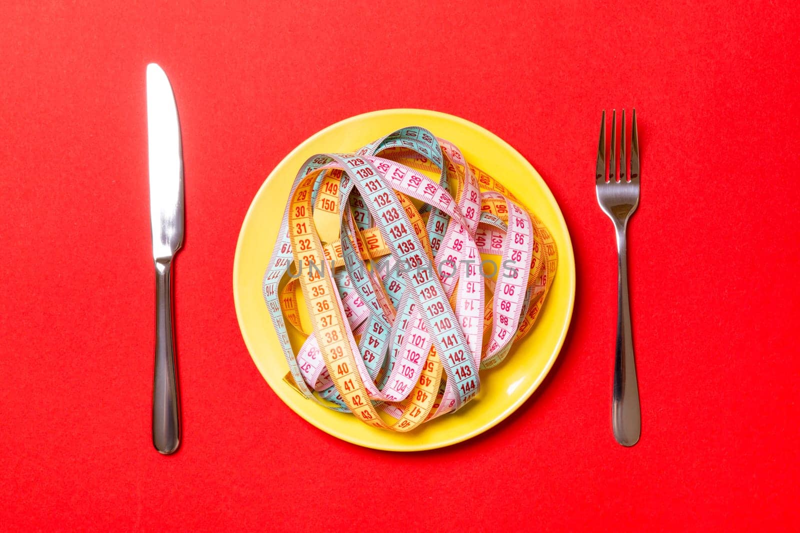 Top view of heap of colorful measuring tapes in plate on red background. Diet concept with copy space.