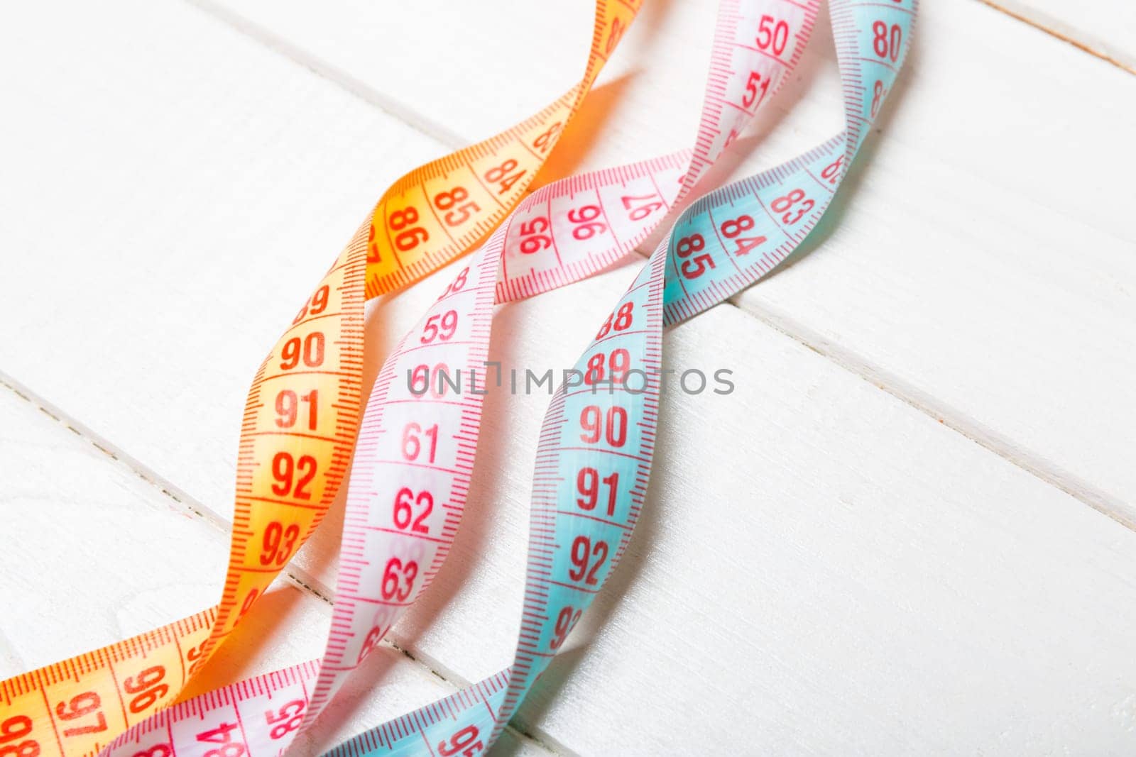 Close up of colorful measure tapes on wooden background. Perfect female figure measurements concept.