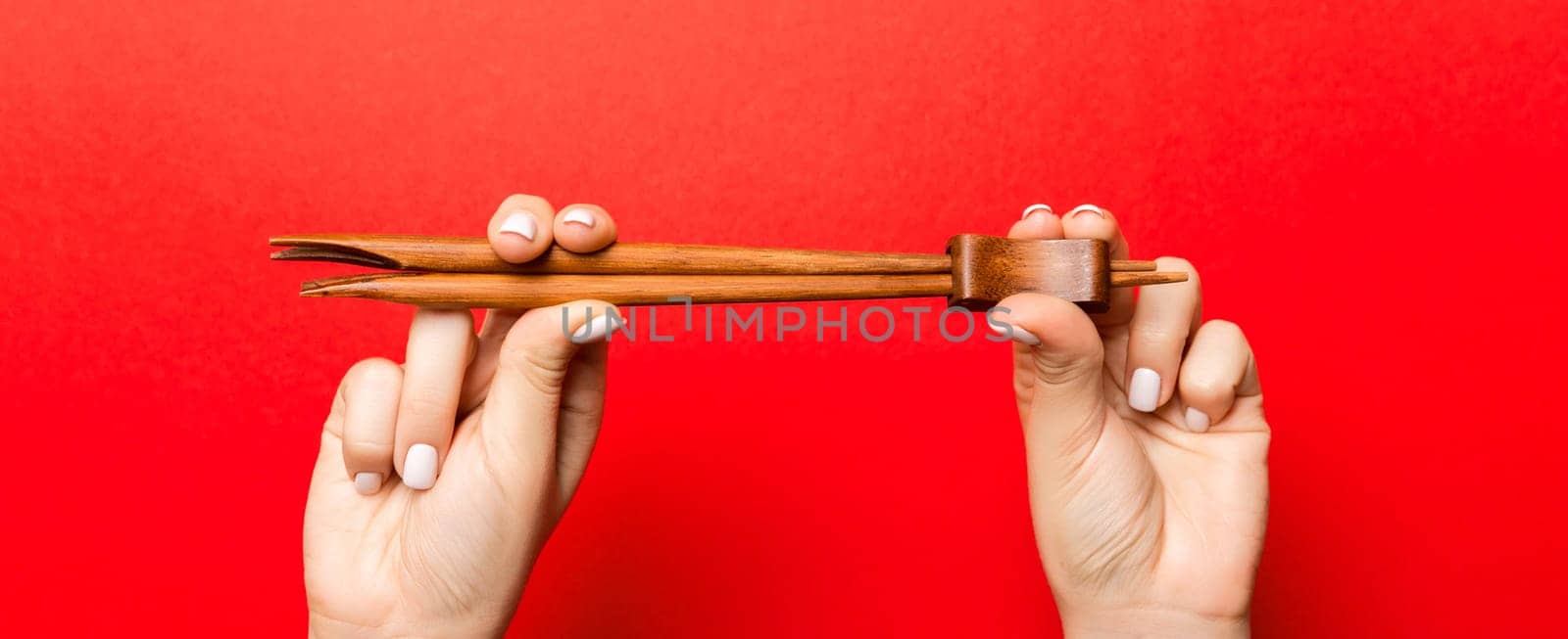 Crop image of two female hands holding chopsticks on red background. Ready to eat concept with copy space by Snegok1967