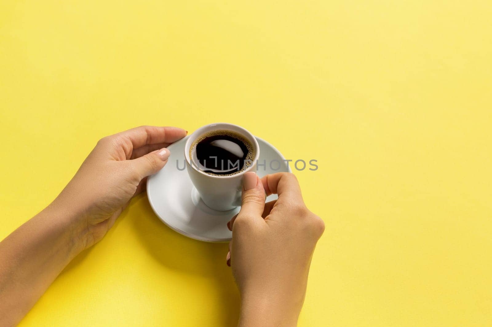 High angle of woman hands holding coffee cup on yellow background Minimalistic style. Flat lay, top view isolated.