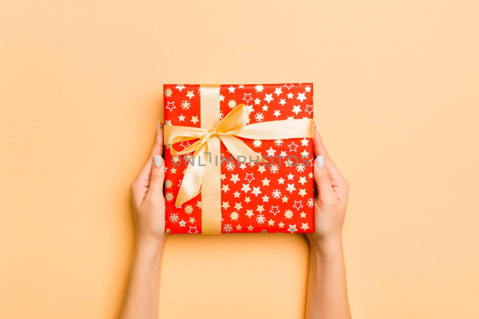 Flat lay of woman hands holding gift wrapped and decorated with bow on gold background with copy space. Christmas and holiday concept.