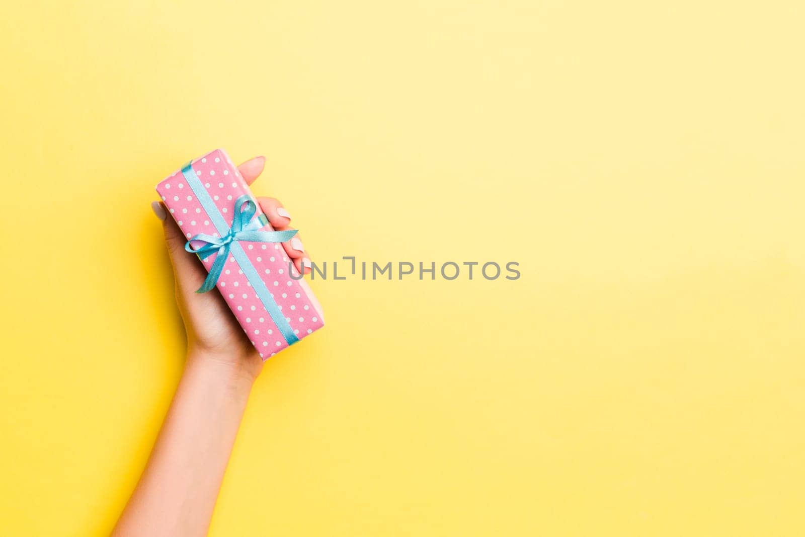 Woman arms holding gift box with colored ribbon on yellow table background, top view and copy space for you design.