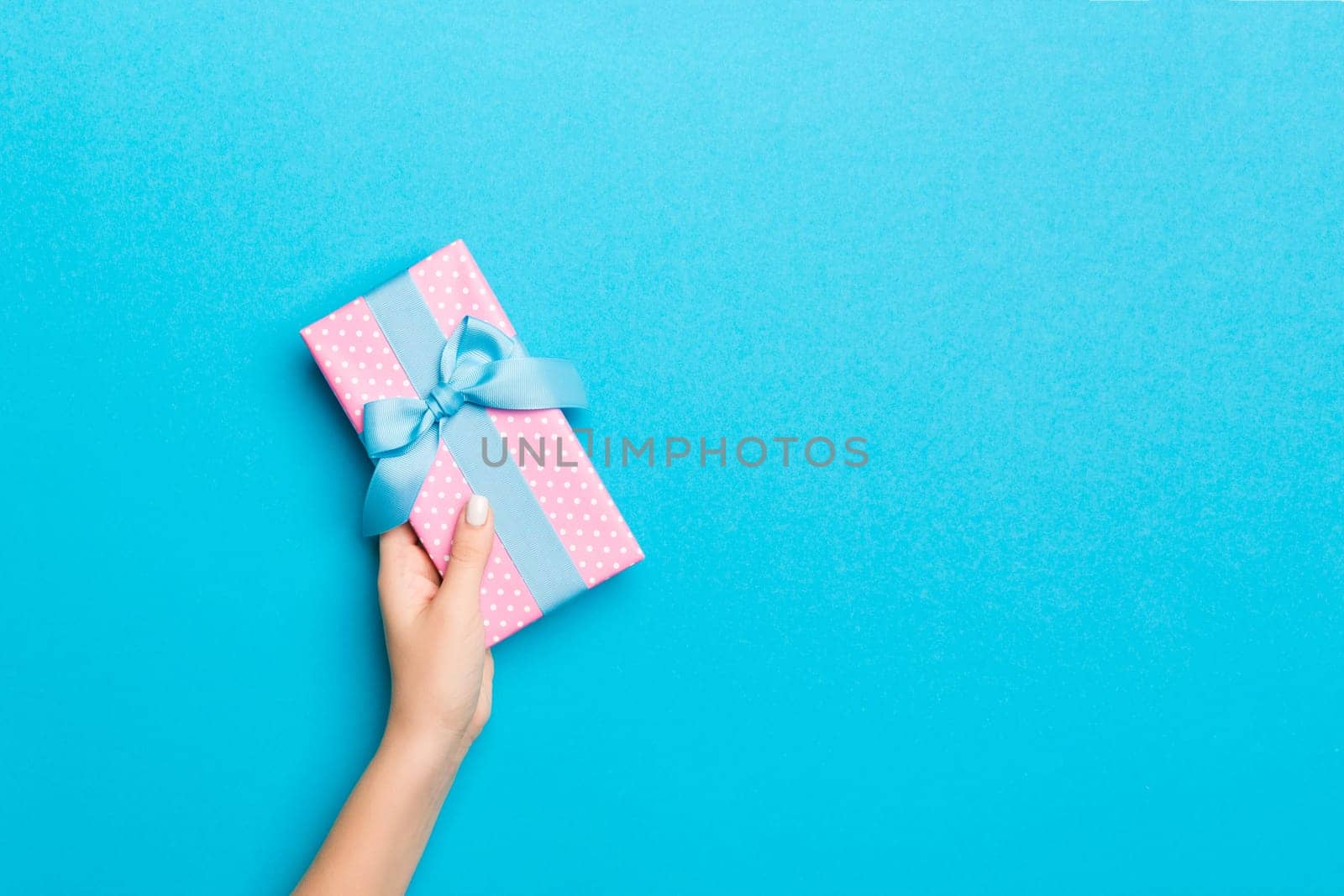 Woman arms holding gift box with colored ribbon on blue table background, top view and copy space for you design.