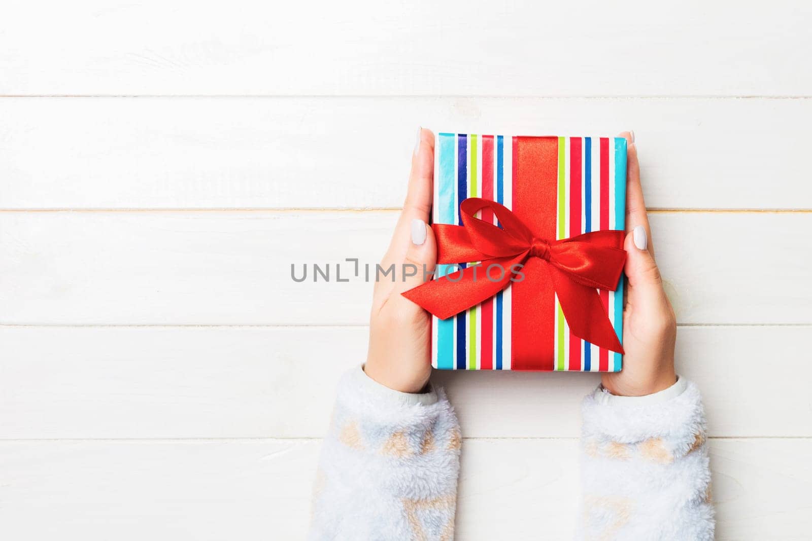 Flat lay of woman hands holding gift wrapped and decorated with bow on white wooden background with copy space. Christmas and holiday concept.