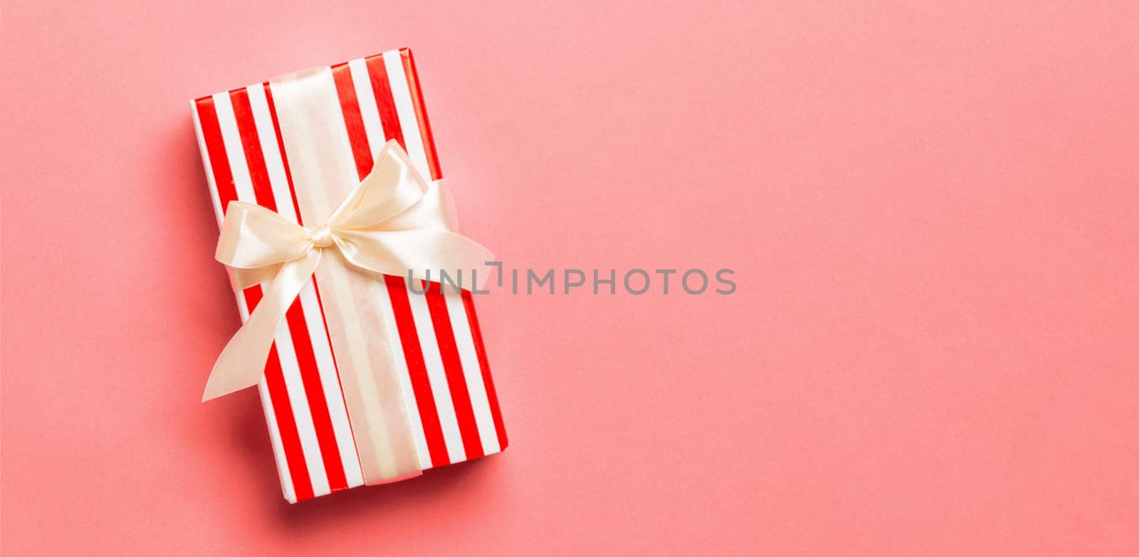 wrapped Christmas or other holiday handmade present in paper with yellow ribbon on living coral background. Present box, decoration of gift on colored table, top view with copy space.