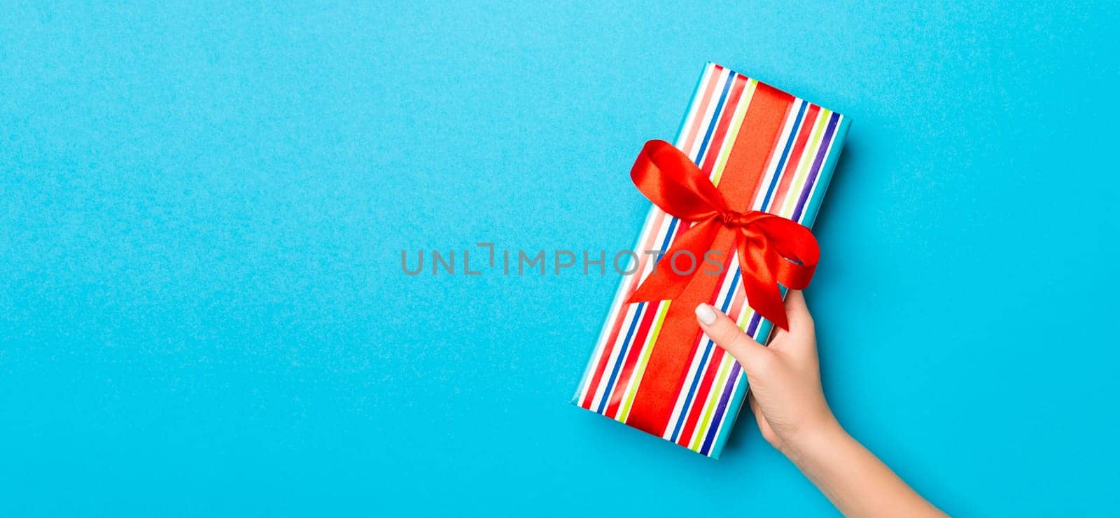 Woman arms holding gift box with colored ribbon on blue table background, top view and copy space for you design.