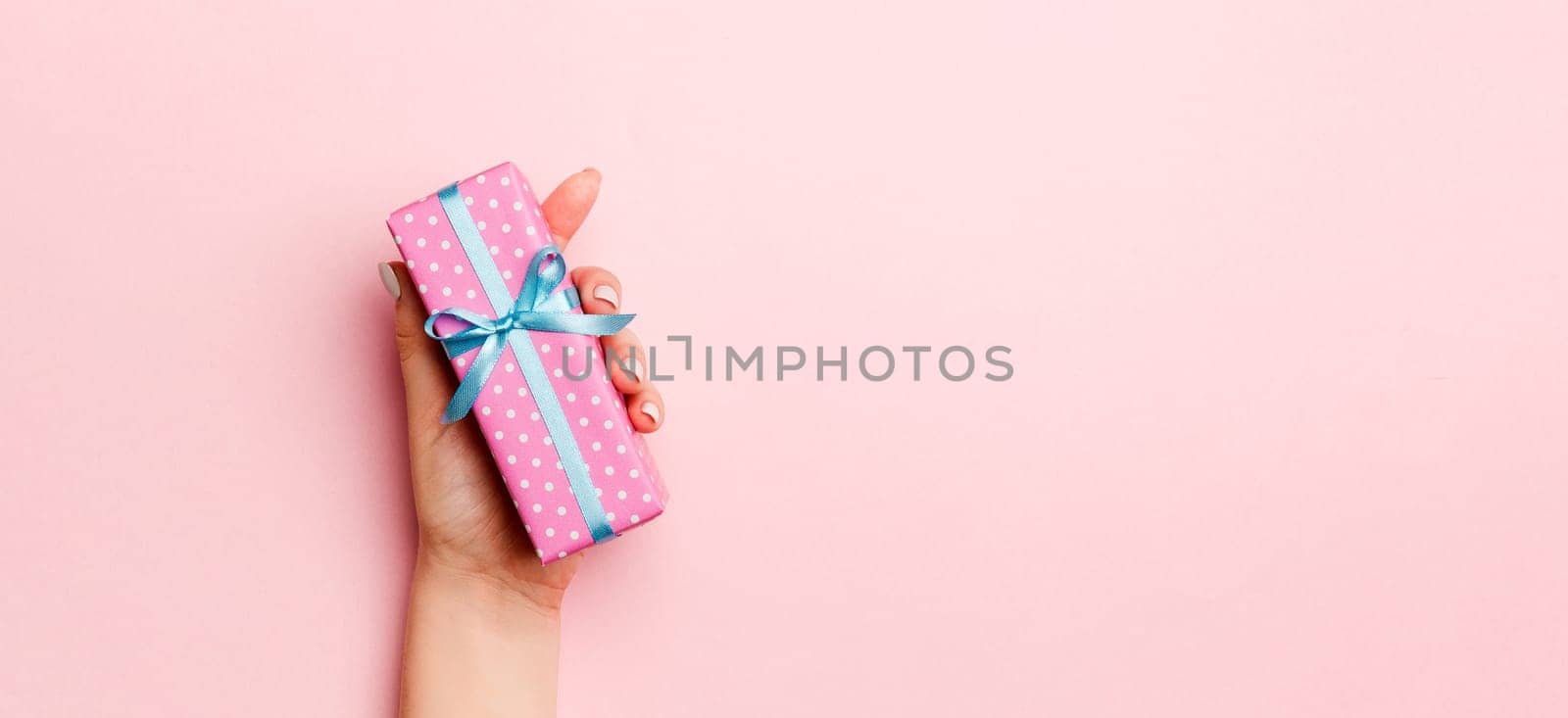 Female's hands holding striped gift box with colored ribbon on living coral background. Christmas concept or other holiday handmade present box, concept top view with copy space.