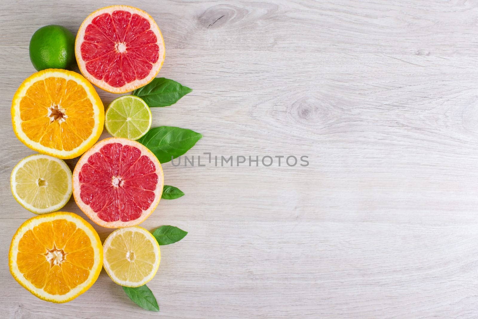 Juicy citrus fruits cut background mint leaf. Oranges, lemons, limes, grapefruit, mint leaves on a bright wooden background.