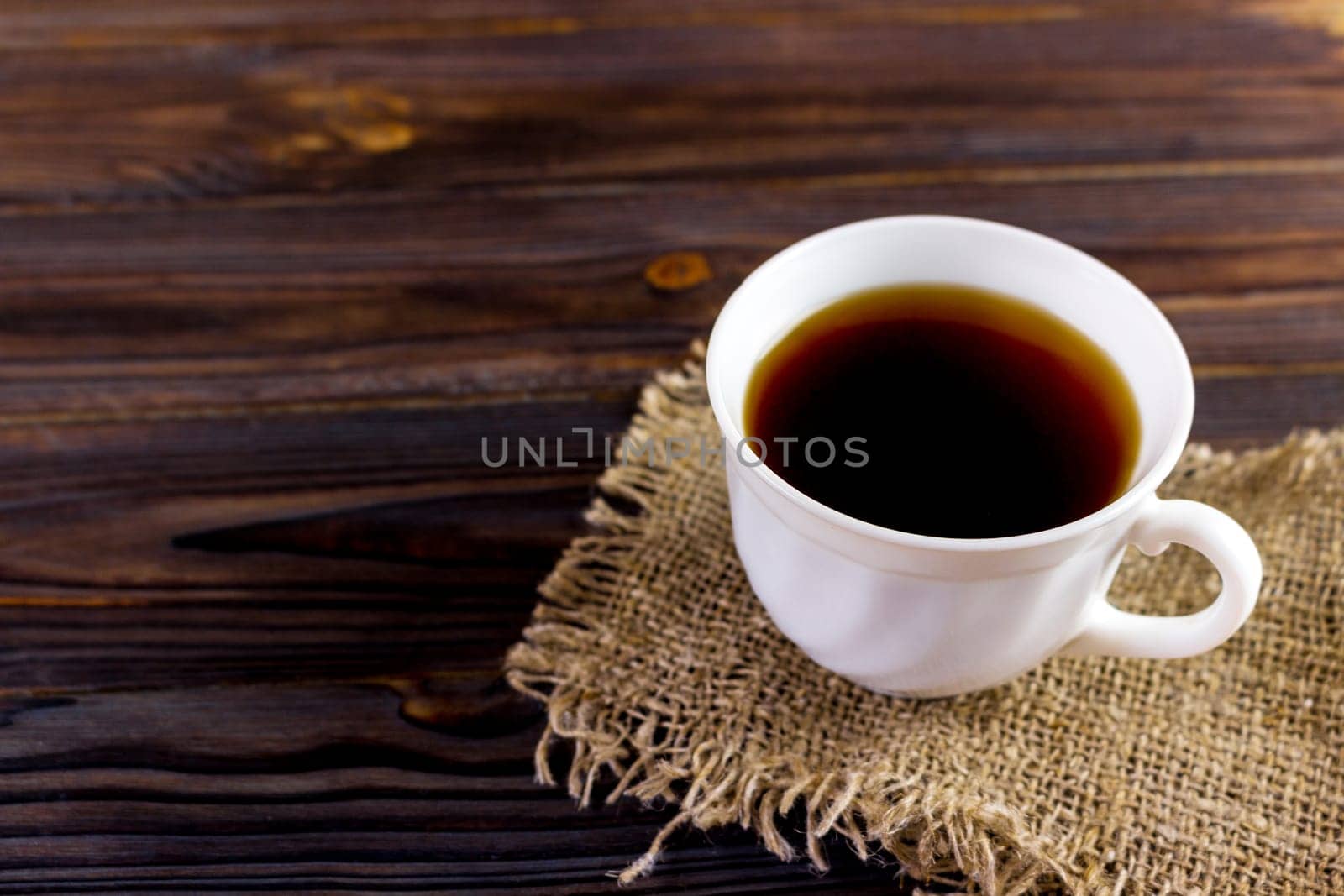 cup of coffee on burlap on wooden background.