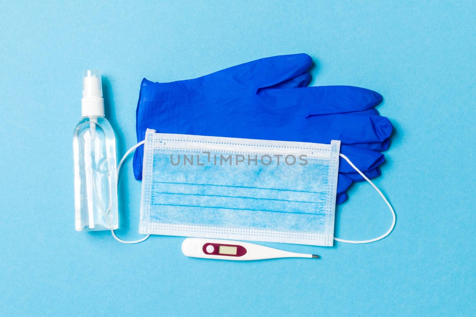Top view of alcohol hand sanitizer, latex gloves, digital thermometer and medical mask on blue background. Virus protection equipment concept with copy space.