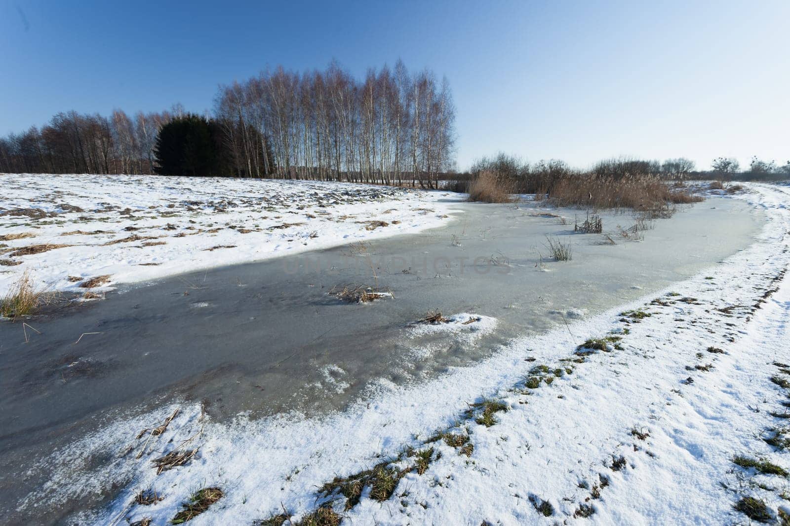 Frozen snow and water on a rural field, sunny winter day
