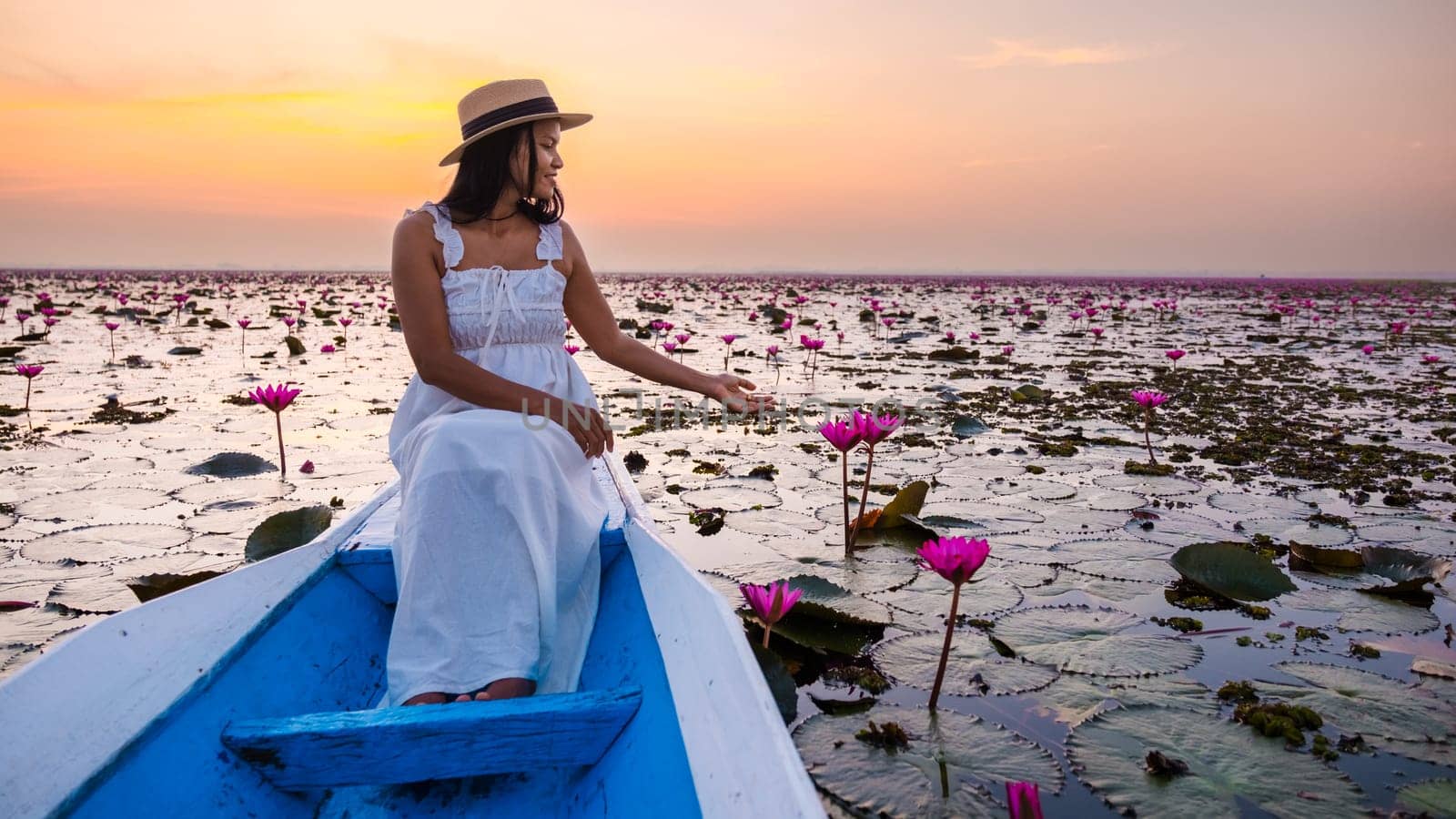 Asian women with a hat and dress in a boat at the Beautiful Red Lotus Sea Kumphawapi is full of pink flowers in Udon Thani in northern Thailand. Flora of Southeast Asia.