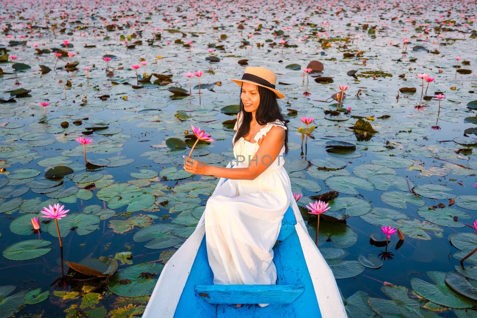 Asian women with a hat and dress in a boat at the Beautiful Red Lotus Sea Kumphawapi is full of pink flowers in Udon Thani in northern Thailand. Flora of Southeast Asia.