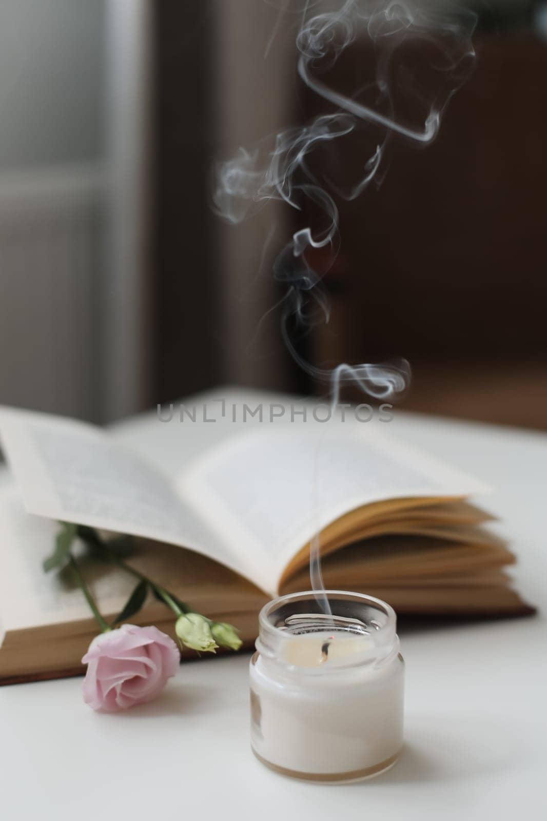 Still life details in home interior of living room. Eco-friendly fragrance for the home. Cozy home concept. Open book with flower, burning candle with smoke