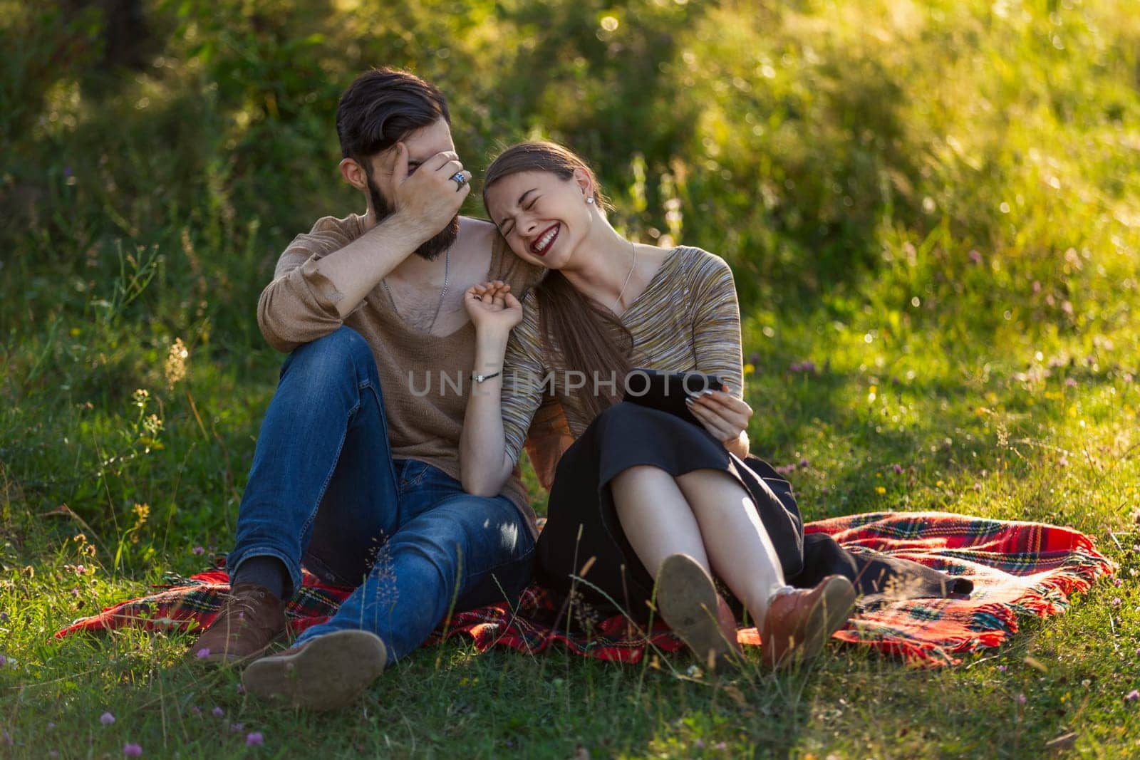 Young couple sitting in nature and looking at a tablet by zokov