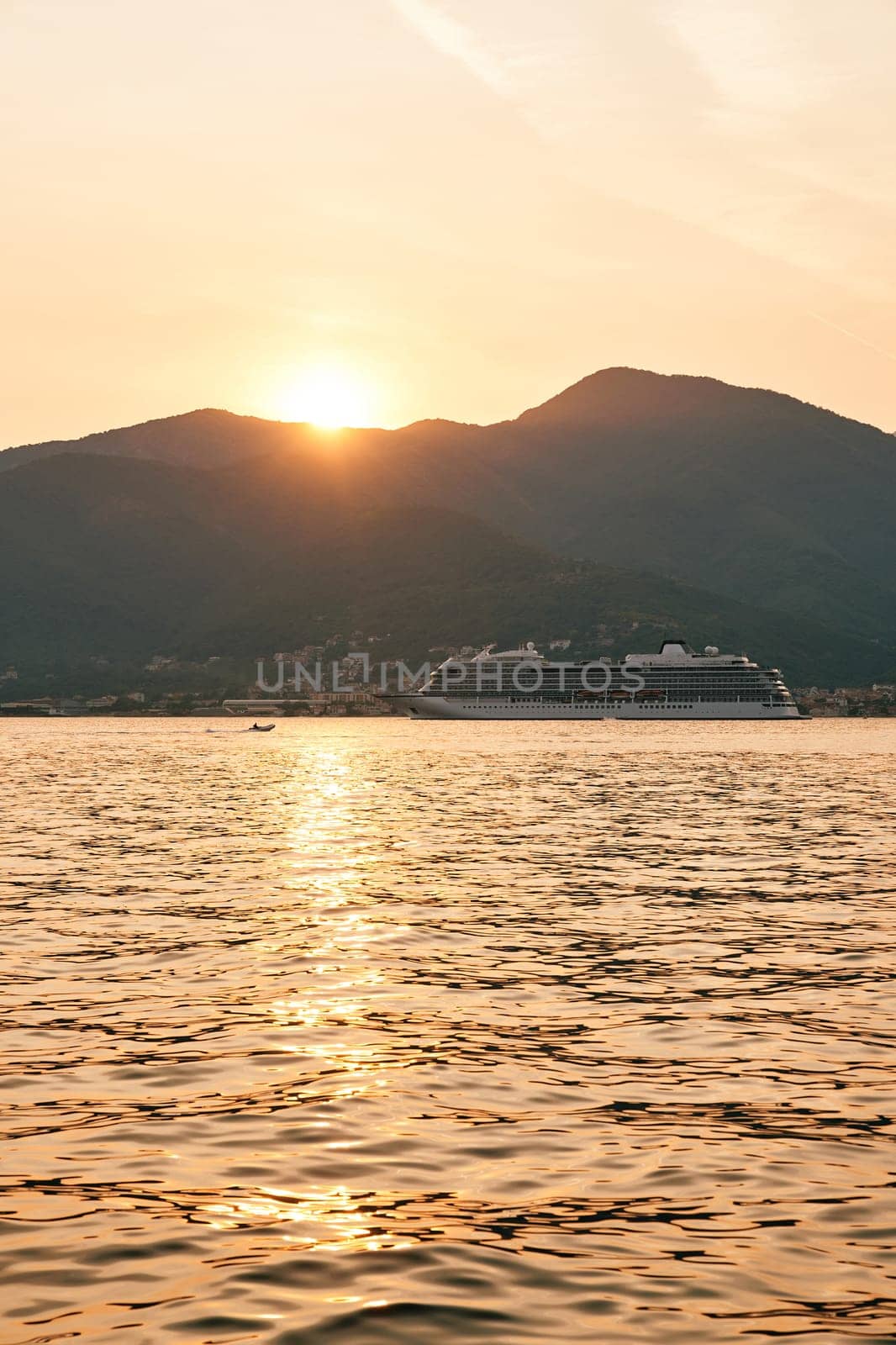 White cruise ship sails on the sea against the backdrop of mountains at sunset by Nadtochiy