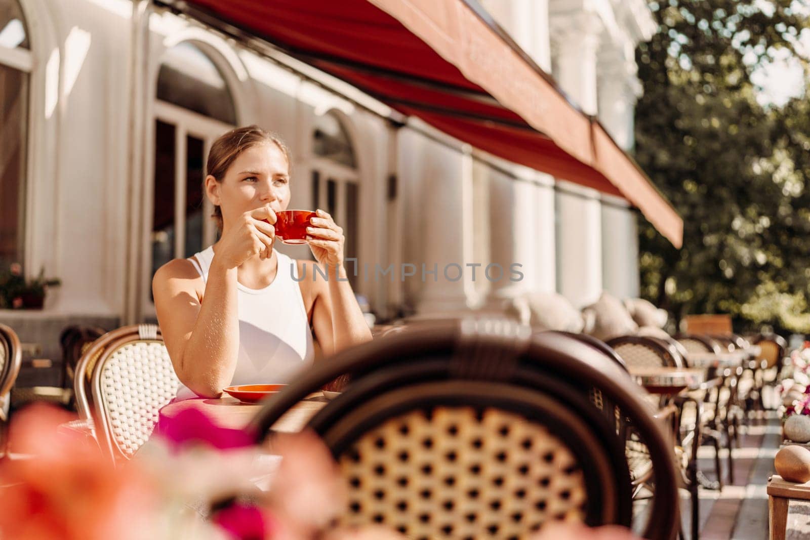 Portrait of happy woman sitting in a cafe outdoor drinking coffee. Woman while relaxing in cafe at table on street, dressed in a white T-shirt and jeans by Matiunina