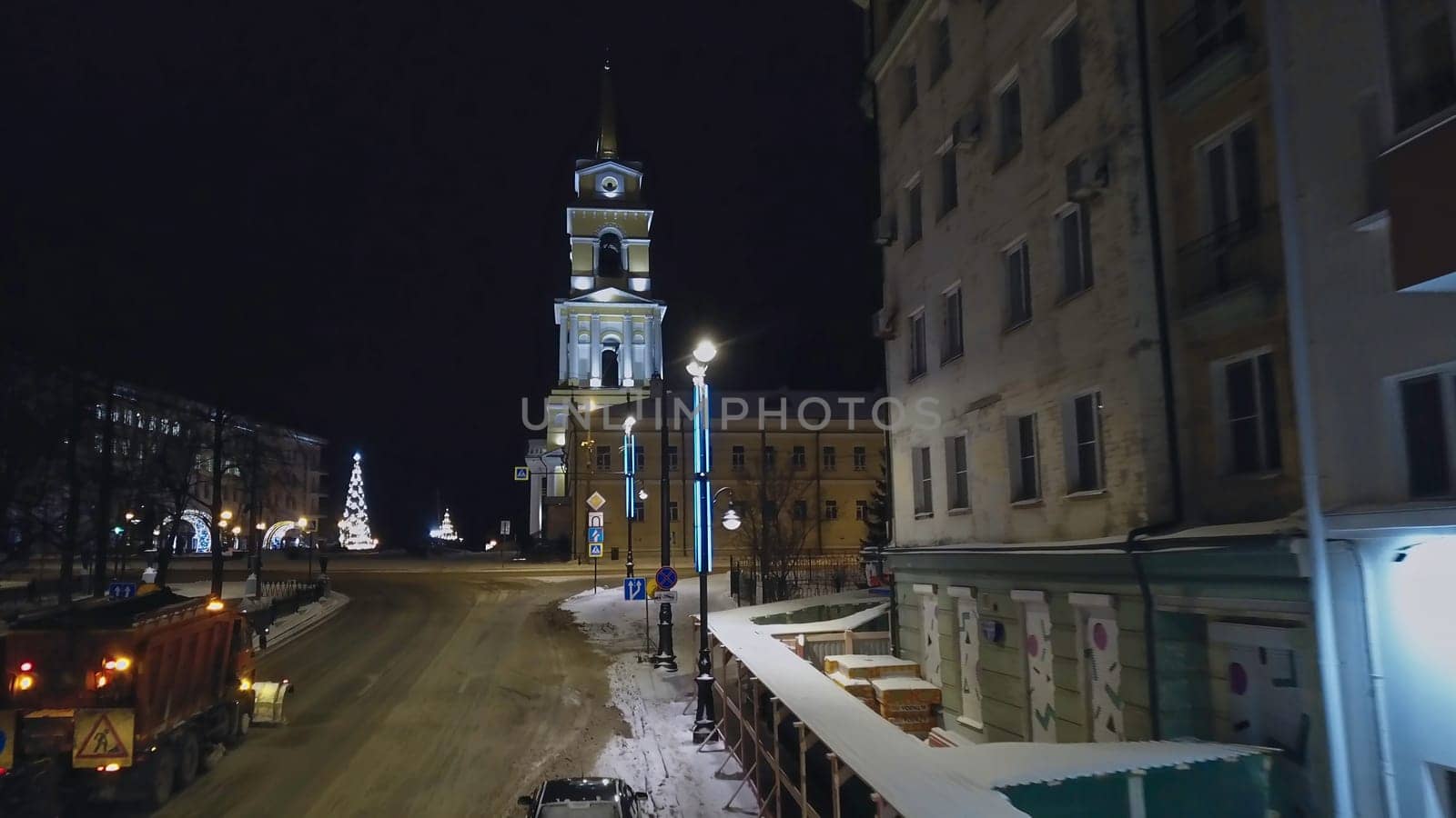 Winter evening landscape of the city. Clip. A street with tall residential buildings next to a road with cars on which lanterns shine and a white temple is visible. High quality 4k footage