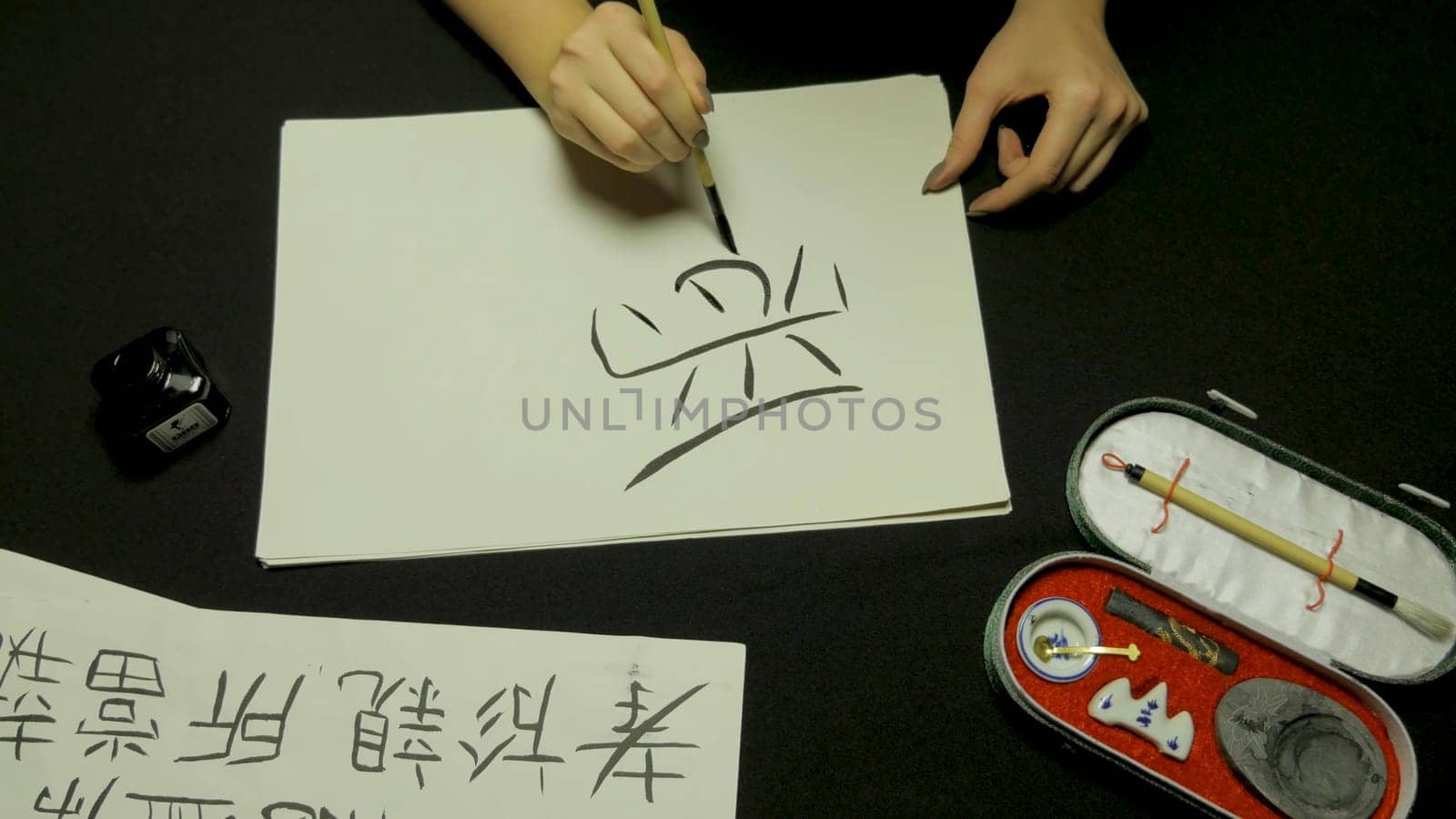 Woman's hand writing chinese calligraphy. Female hand holding a writing brush Chinese characters.