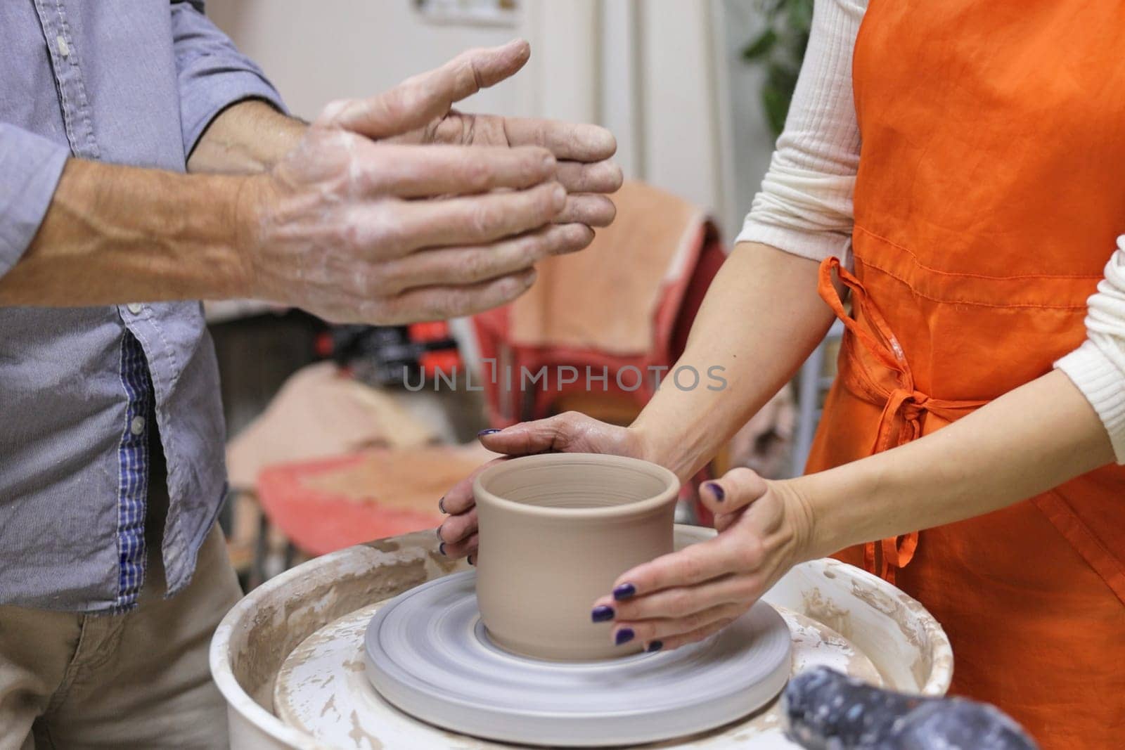 potter helps woman to work with the ceramic wheel and making a cup from clay pot