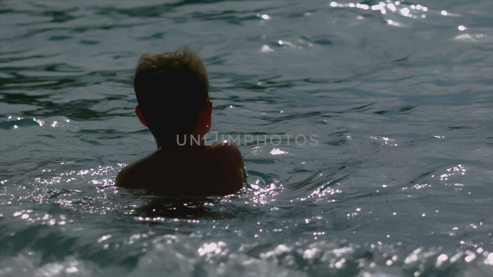 Boy swims in sea with waves. Creative. Boy swims alone on sea in sunny weather. Boy is resting on sea and swimming with waves and splashes.