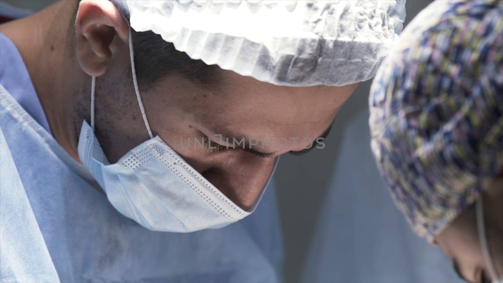 Close up of heads of male surgeons wearing protective masks surgical caps in a hospital operating theater. Concept of medicine and health.