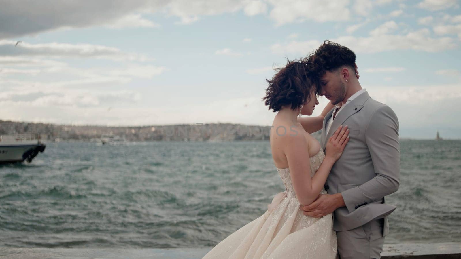 Cute newlywed couple embracing at the beach on their wedding day. Action. Bride and groom in love by the sea standing on pier
