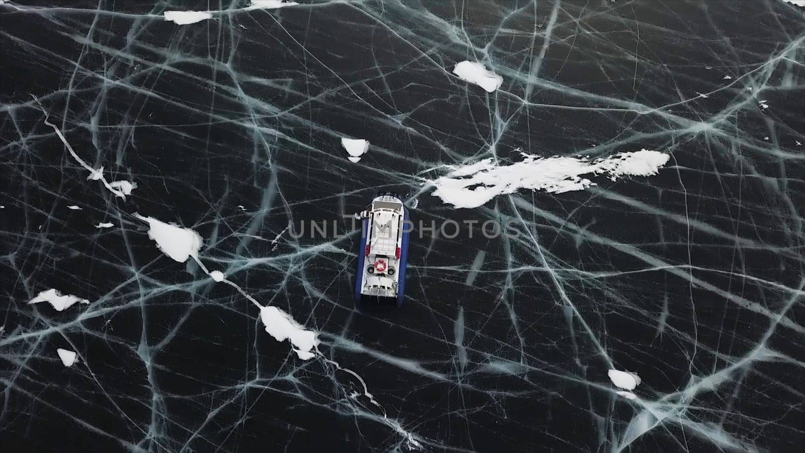 Aerial view of sliding hovercraft on frozen beautiful Baikal lake. Top view of the reservoir surface bound by thick cracked ice and a moving hovercraft.