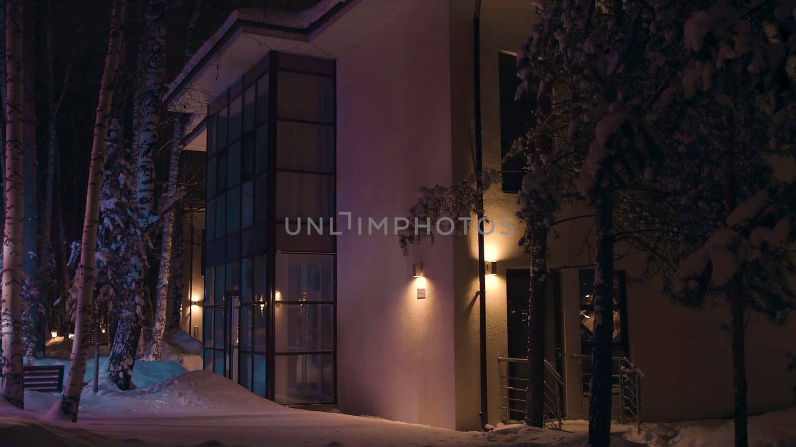 Facade of the big house in the late winter evening illuminated by colorful flashing light of an emergency car. Outdoors view of the cottage in snowy winter at night.