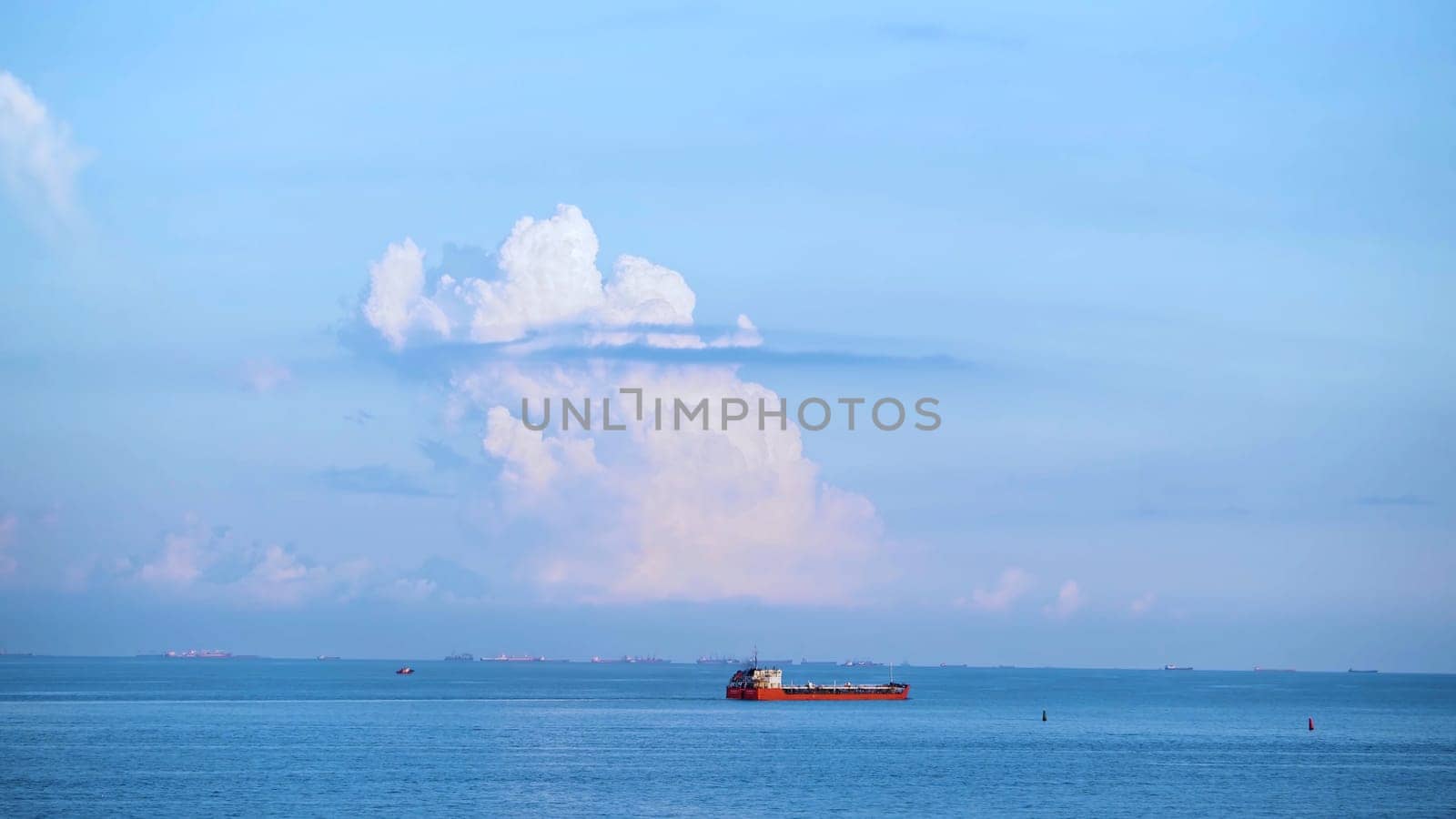 Breathtaking seascpe with a sailing red barge on blue cloudy sky on the background, water transport concept. Cargo ship barge on the sea horizon in a summer sunny day.