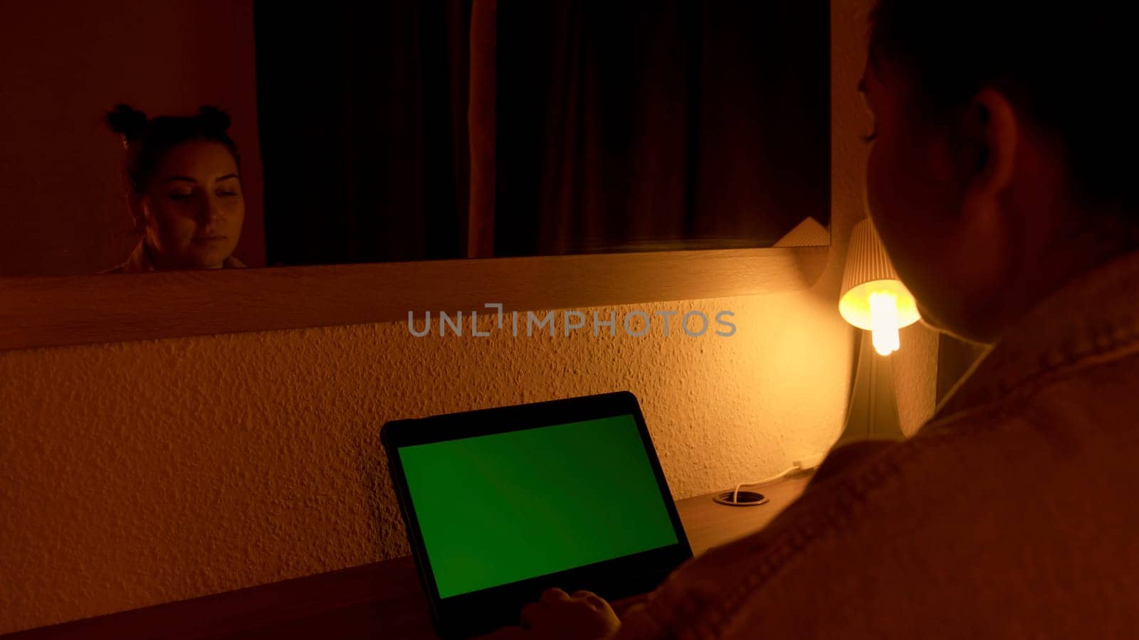 Woman looking at laptop with green screen during night time in front of mirror. Media. Freelancer watching monitor display with chroma key screen, working overtime concept