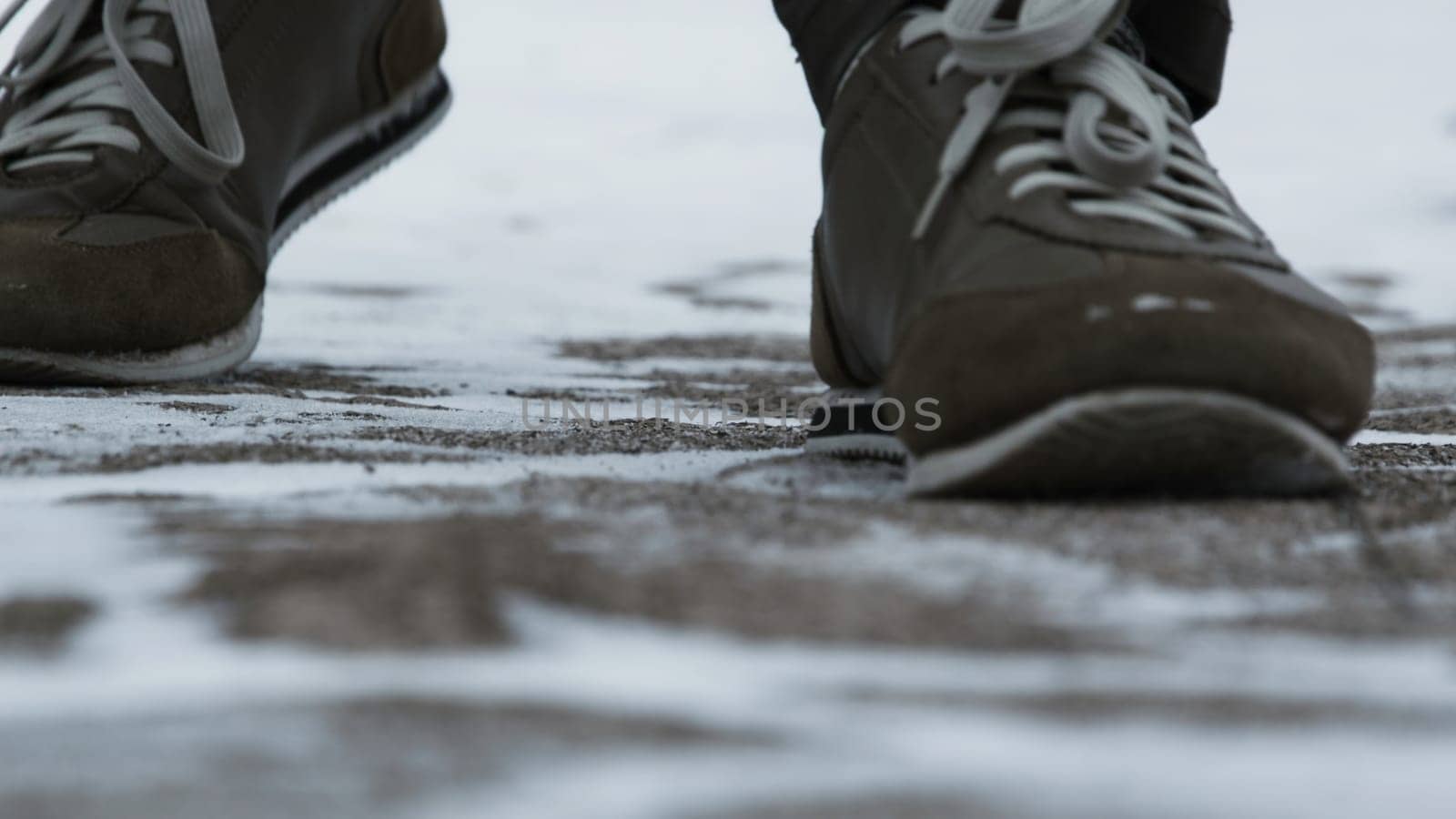Close-up of male legs in winter shoes walking on snow. View of walking on snow with Snow shoes and Shoe spikes in winter. Men's legs in boots close up the snow-covered path in the winter forest.