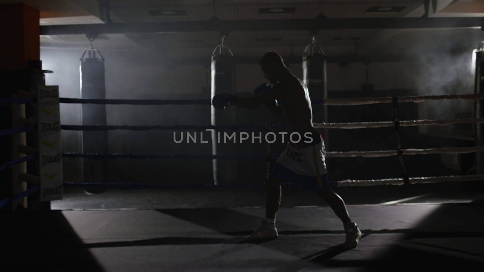 Fighter shadowboxing on training ring. Professional fighter. Male boxer in training sportswear, an exercise in sports hall, fight with a shadow in ring, Strike testing 4K