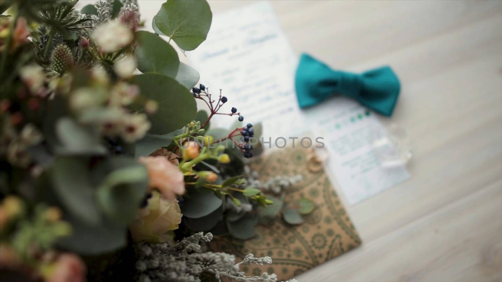 Accessories for the wedding ceremony. Closeup of elegant stylish brown male accessories on wooden background. Top view of bow-tie, belt, floral corsage, golden rings. Wedding bow tai with flower. Preparation for wedding concept