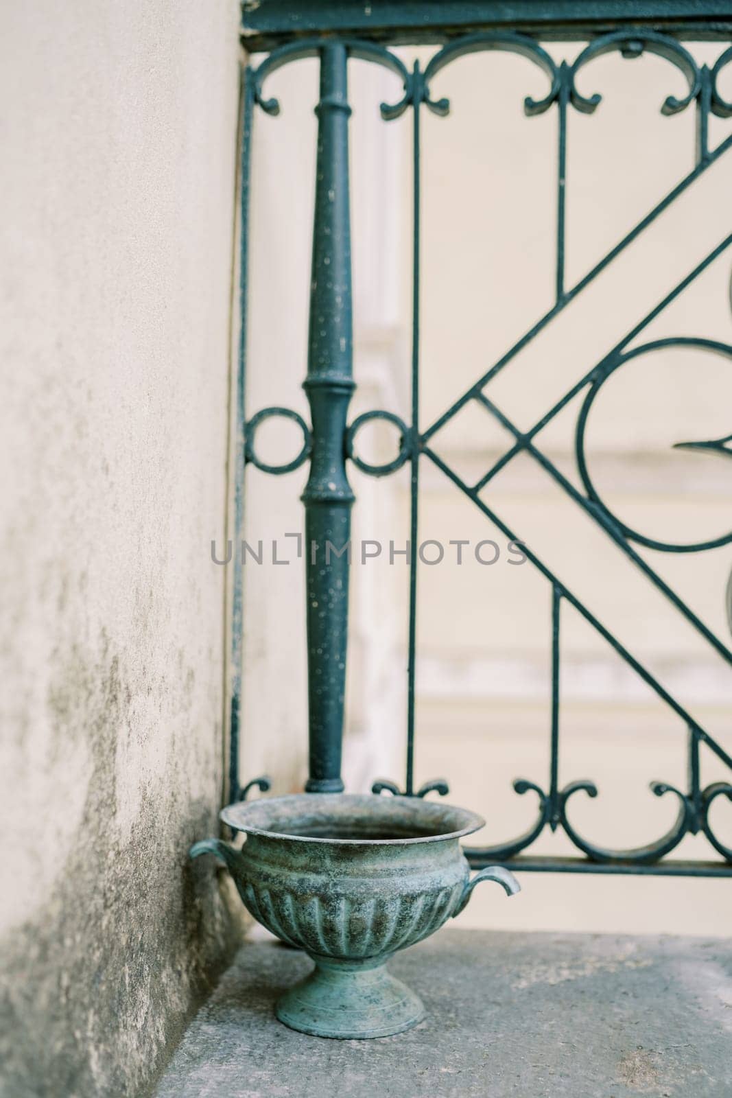 Antique bronze vase stands on the balcony near the wrought iron fence. High quality photo