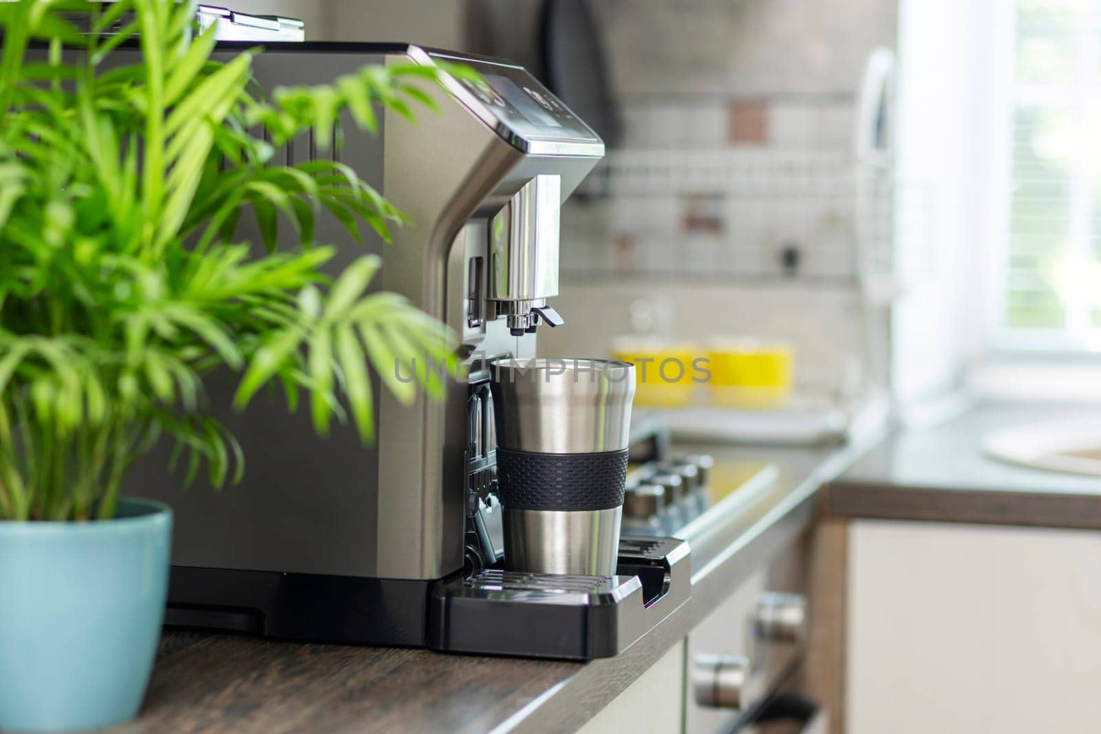 Modern electric coffee machine with cup on countertop in kitchen.