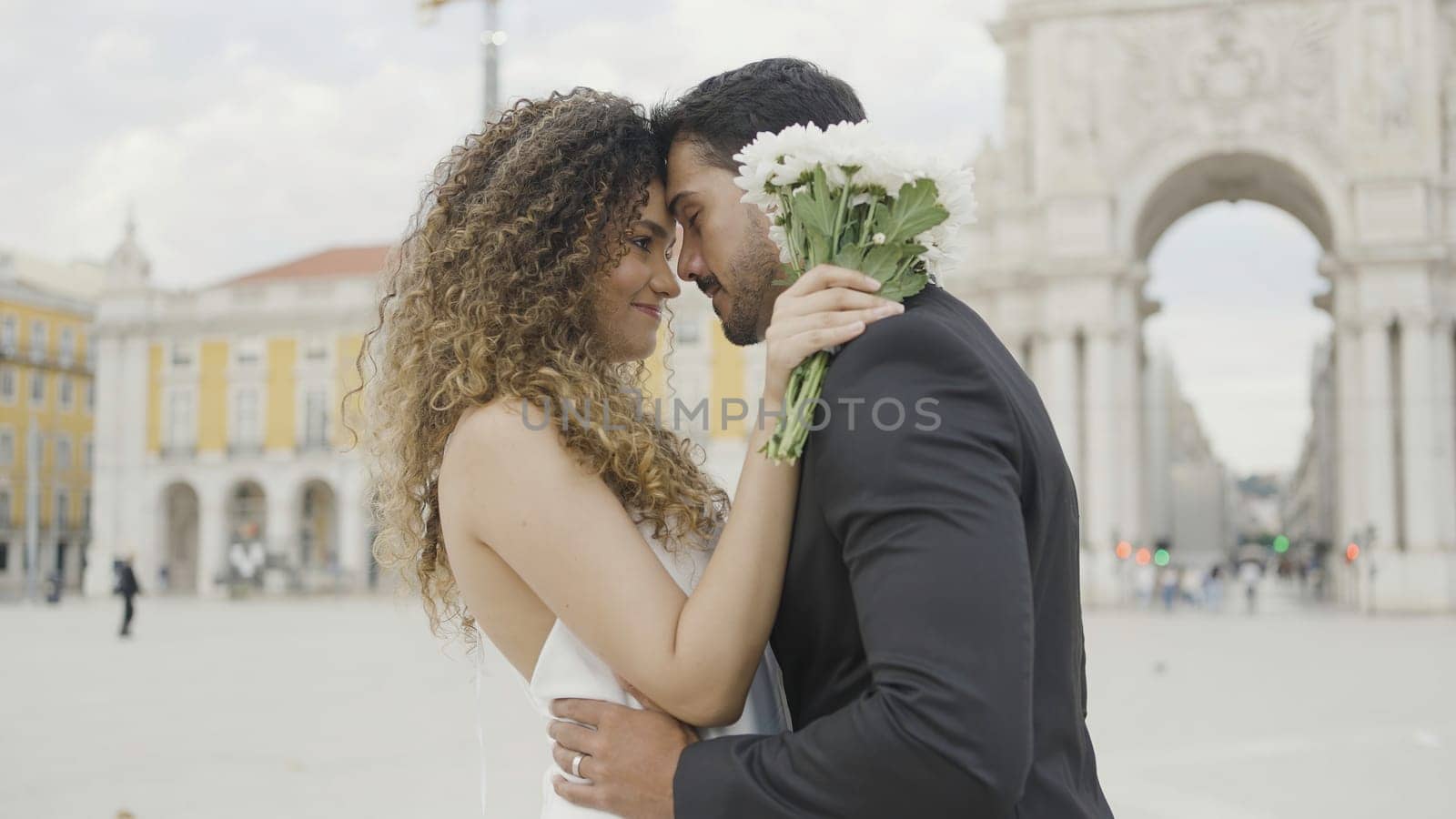 Beautiful couple of lovers tenderly embrace on street. Action. Elegant couple in beautiful outfits are gently embracing. Couple in love in beautiful outfits hugs on city square.