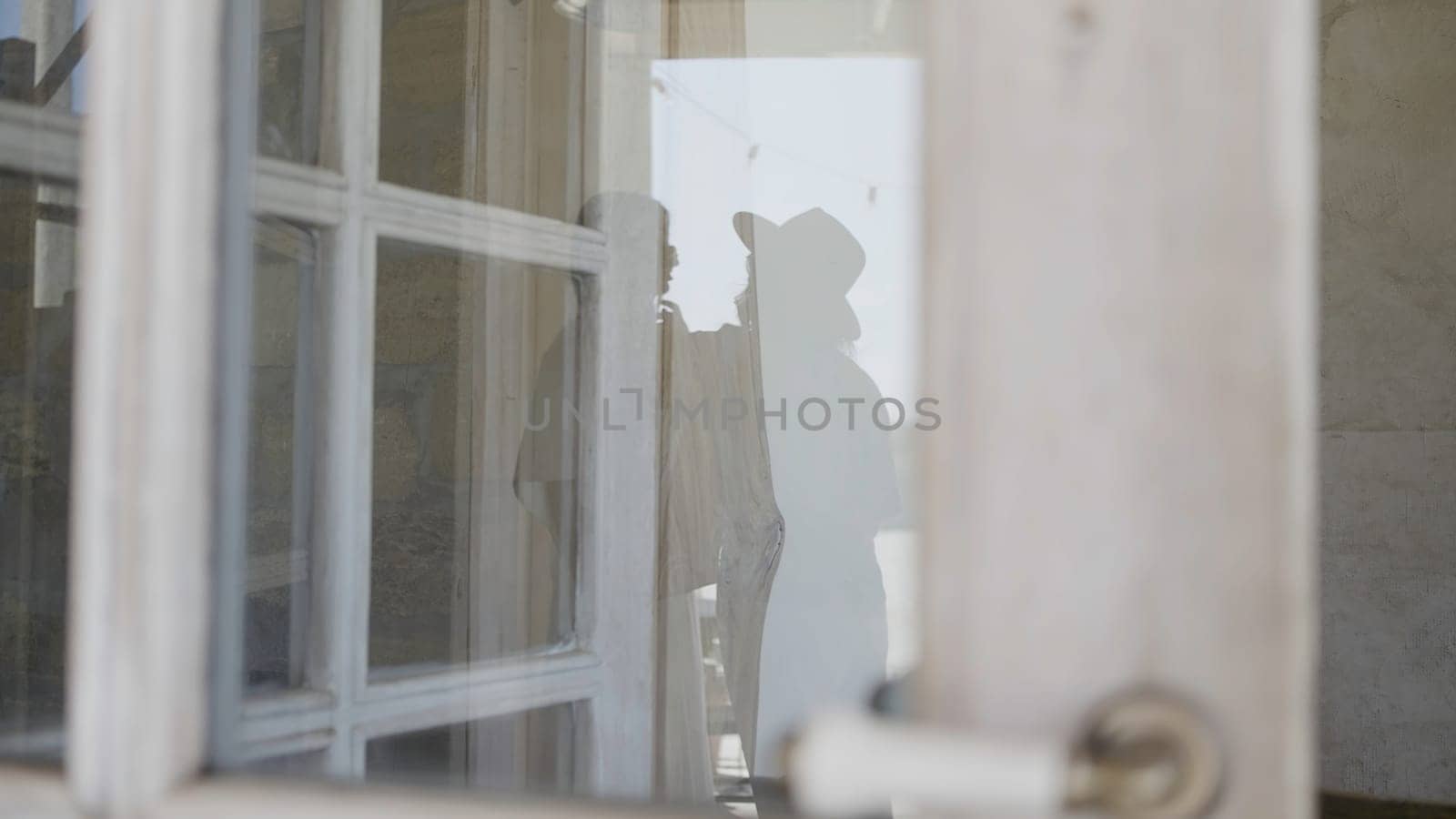View through the window with translucent curtains to the people in a room. Action. Women silhouettes inside the building