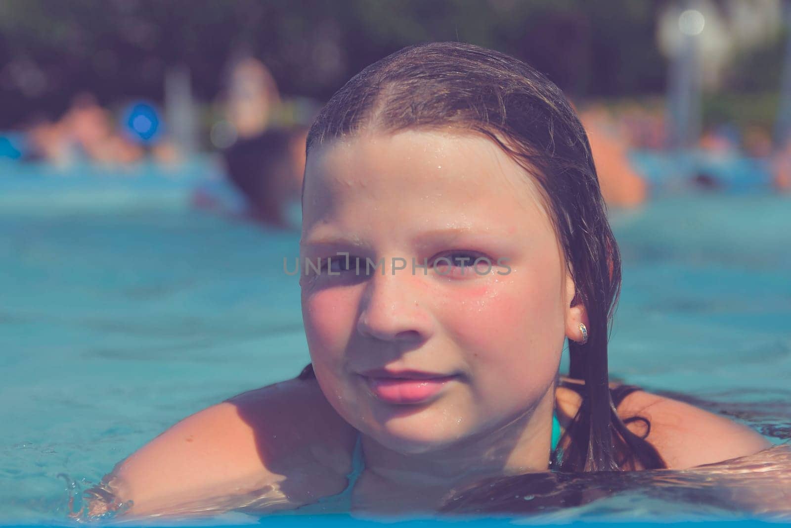 A picture of a little girl at a swimming pool in summer. A small girl swimming to the edge of a swimming pool at a swimming pool. Concept of summer, water fun, sun and relaxation.