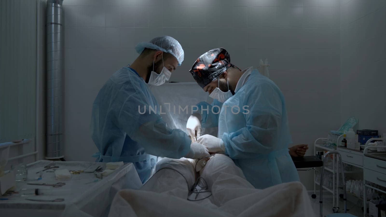Side view of professional surgeon wearing uniform during work with patient in operating theater. Action. Two male surgeons. by Mediawhalestock